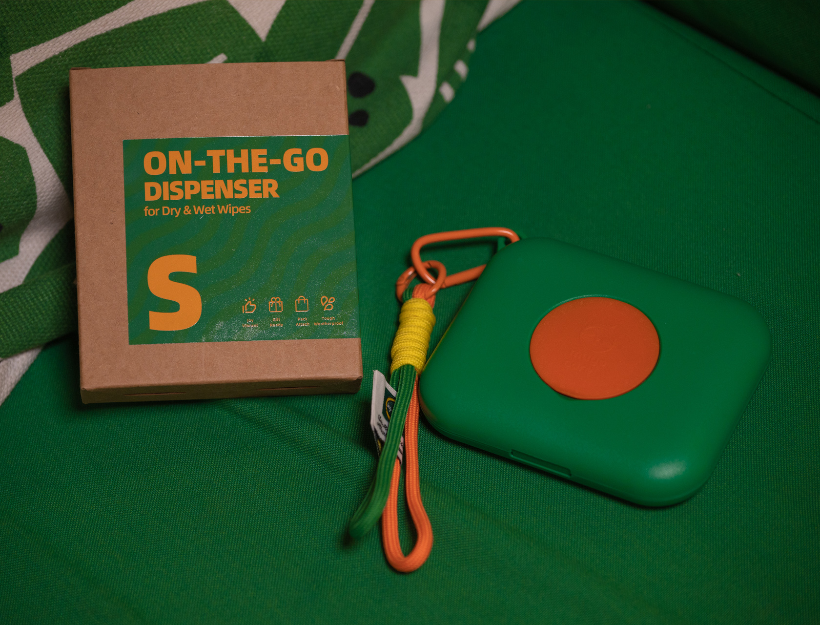 Portable green and orange wet wipe dispenser with keychain attachment for convenience.